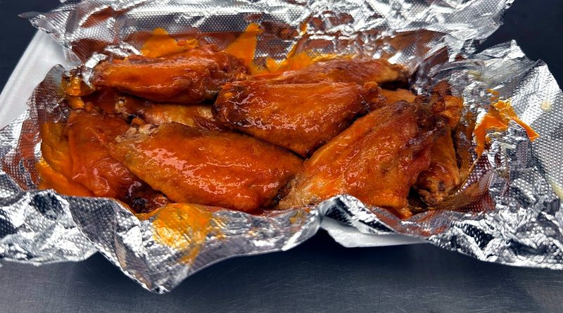 Sauced chicken wings in a foil-lined takeout tray